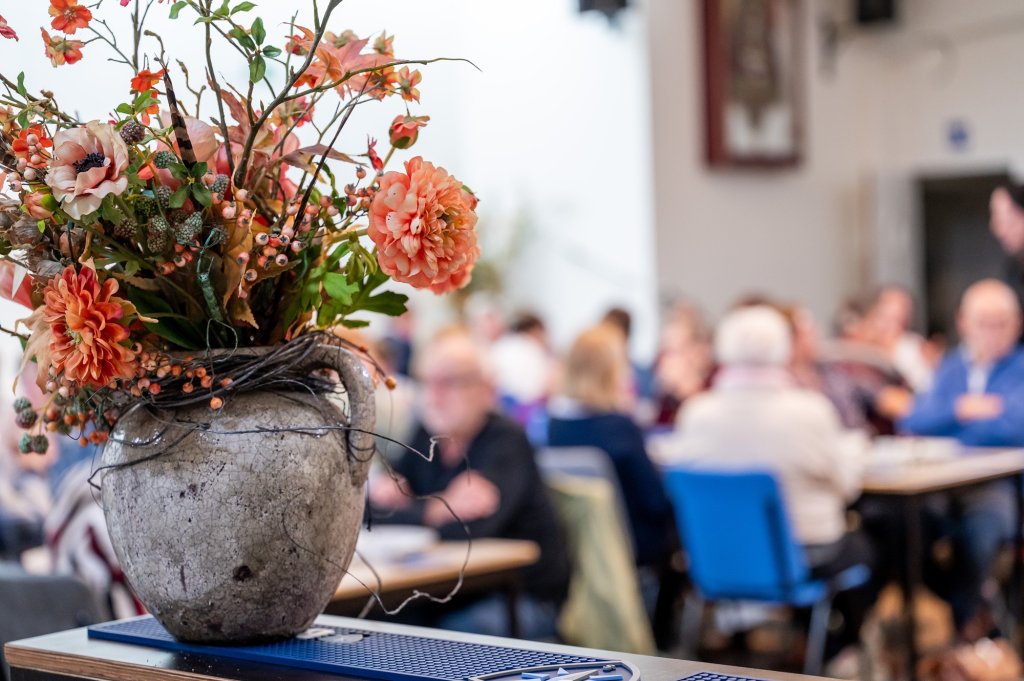 Bloemstuk met op de achtergrond ouderen aan lunchtafels