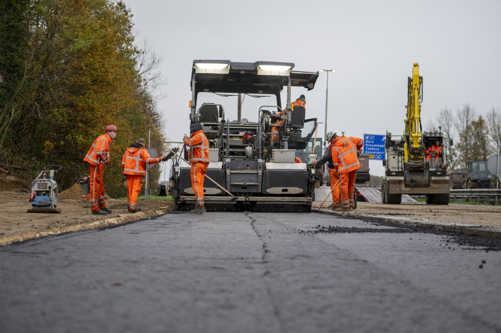 Asfalteervoertuig met enkele werklieden in actie