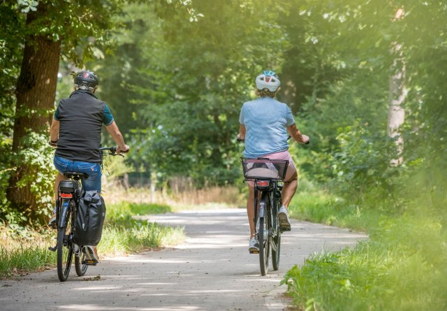 Seniore man en vrouw fietsen op verhard fietspad door de natuur