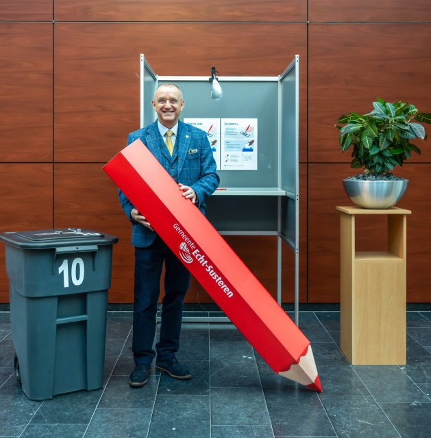 Burgemeester Jos Hessels in stemhokje met grote rode stempotloot in de handen