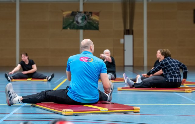 Trainer in sporthal doet op een mat een oefening voor, voor enkele sporters