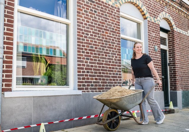 Melanie met kruiwagen zand bij haar geveltuintje