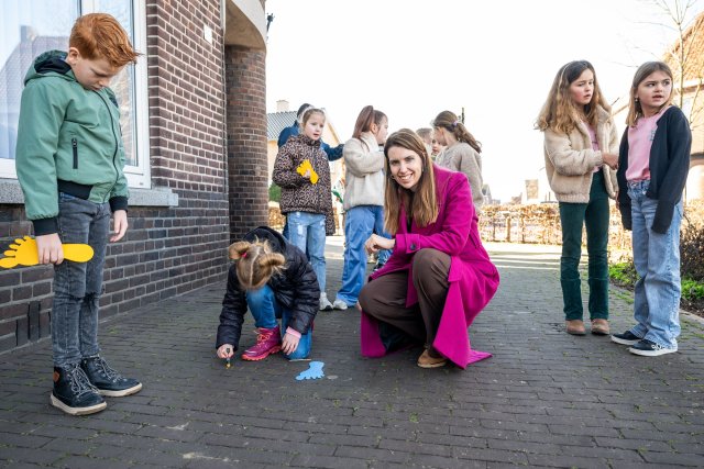 Wethouder Kim Leurs kijkt toe hoe kinderen geschilderde voetjes plaatsen op de stoep