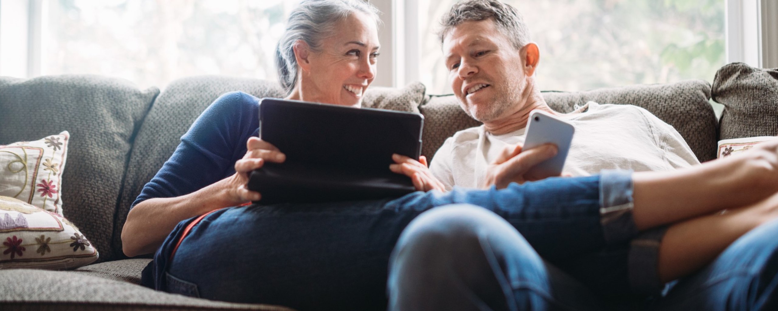 Man en vrouw op de bank met telefoon en tablet in handen