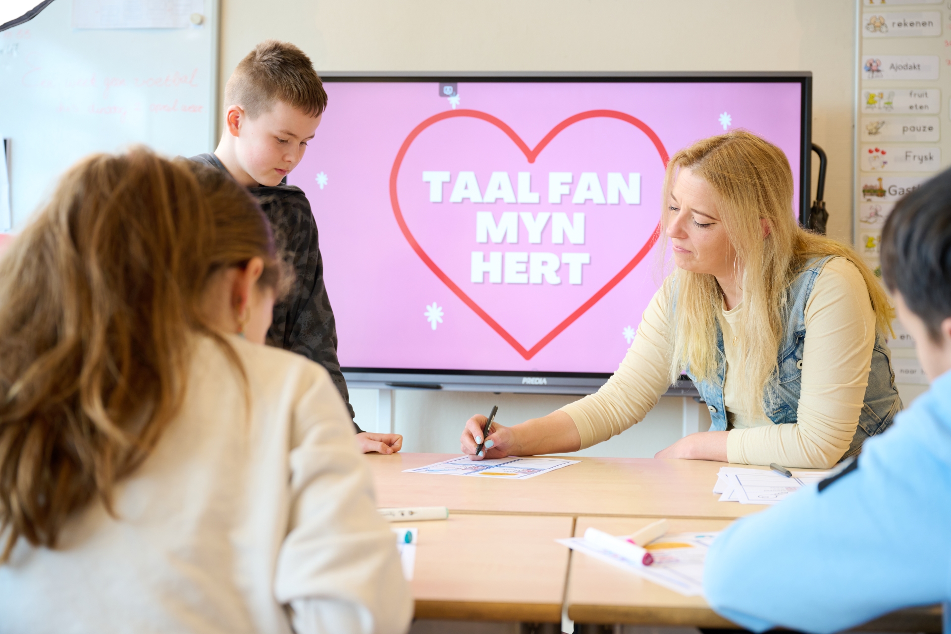 Een aantal jongeren zitten voor een scherm waar een hart met Taal fan myn Hert op staat.
