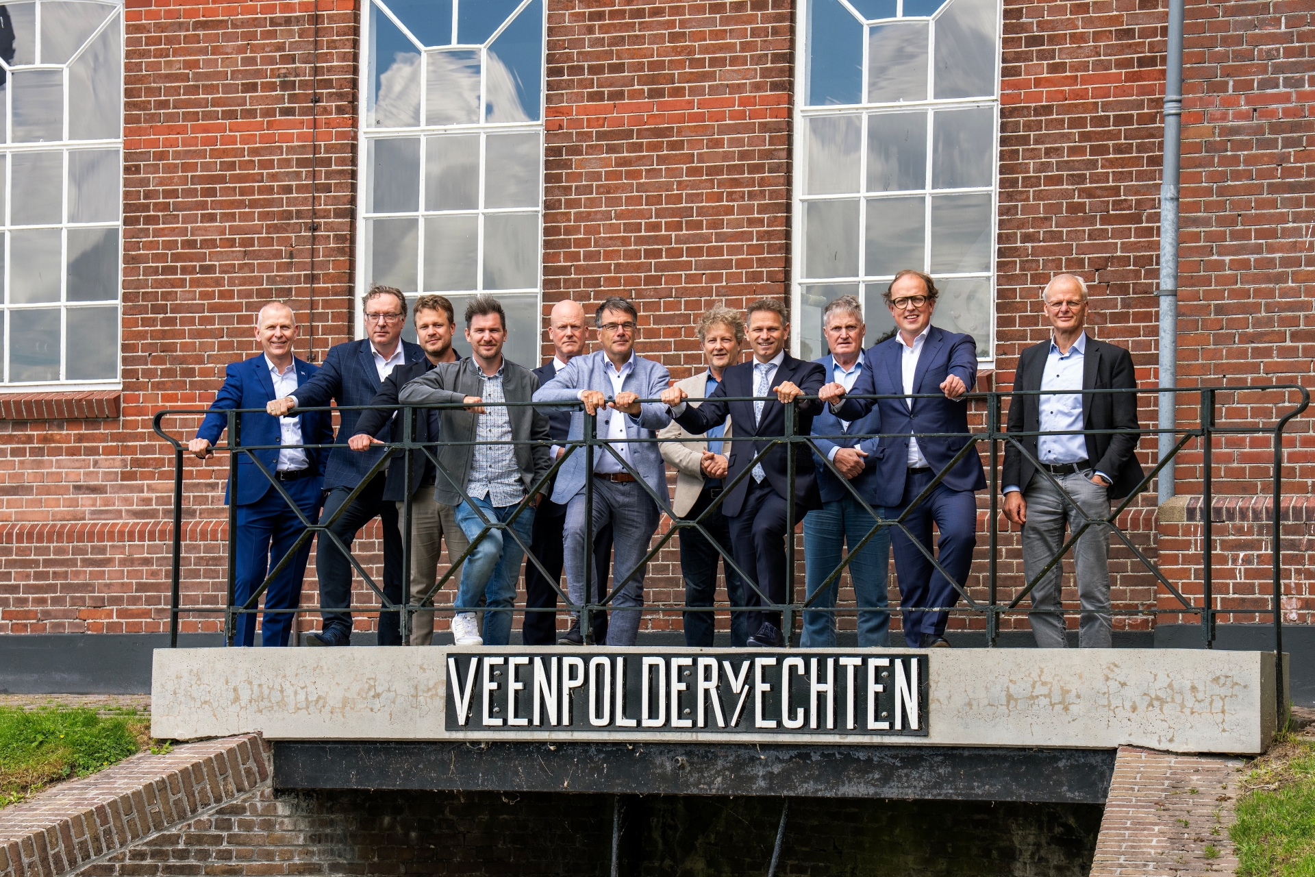 Een hele groep mensen staat op een brugje waar "VEENPOLDER V/ ECHTEN" op staat.