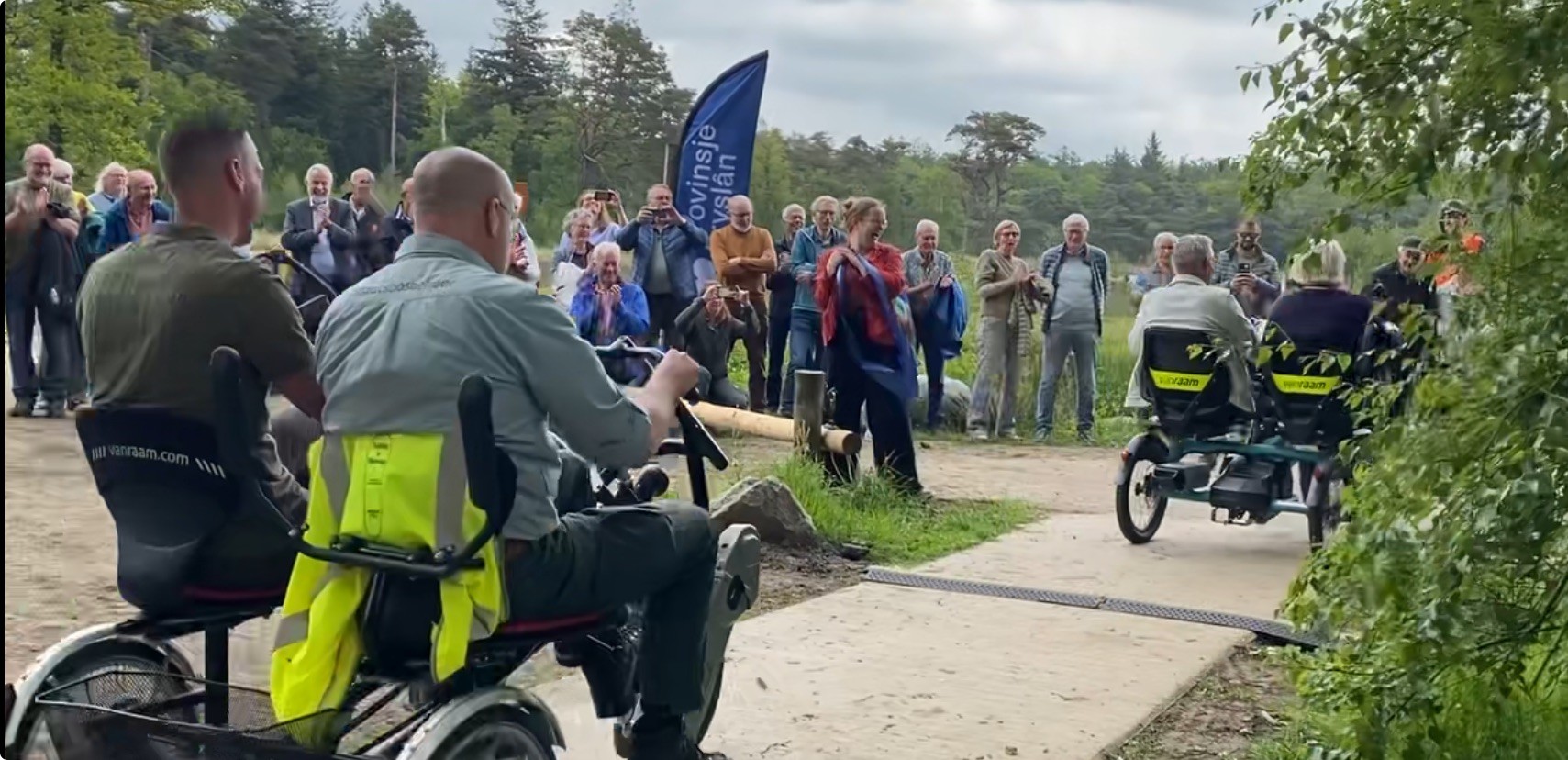 Mensen op duofietsen fietsen over het nieuwe fietspad, publiek juicht het toe.