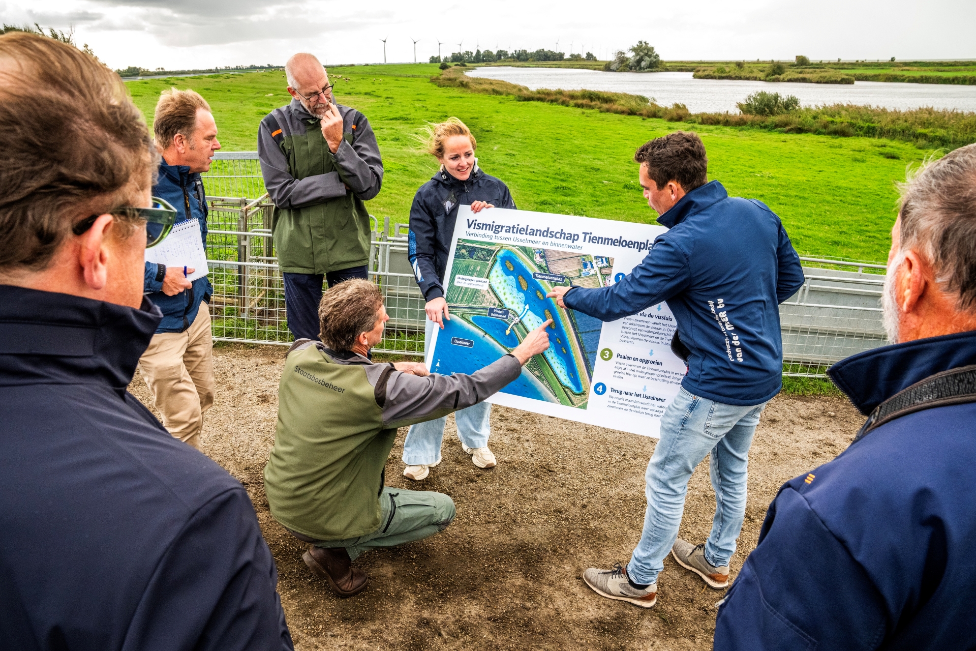 Meerdere personen houden een grote kaart vast waar de Tienmeloenplas op staat en wijzen daarna.