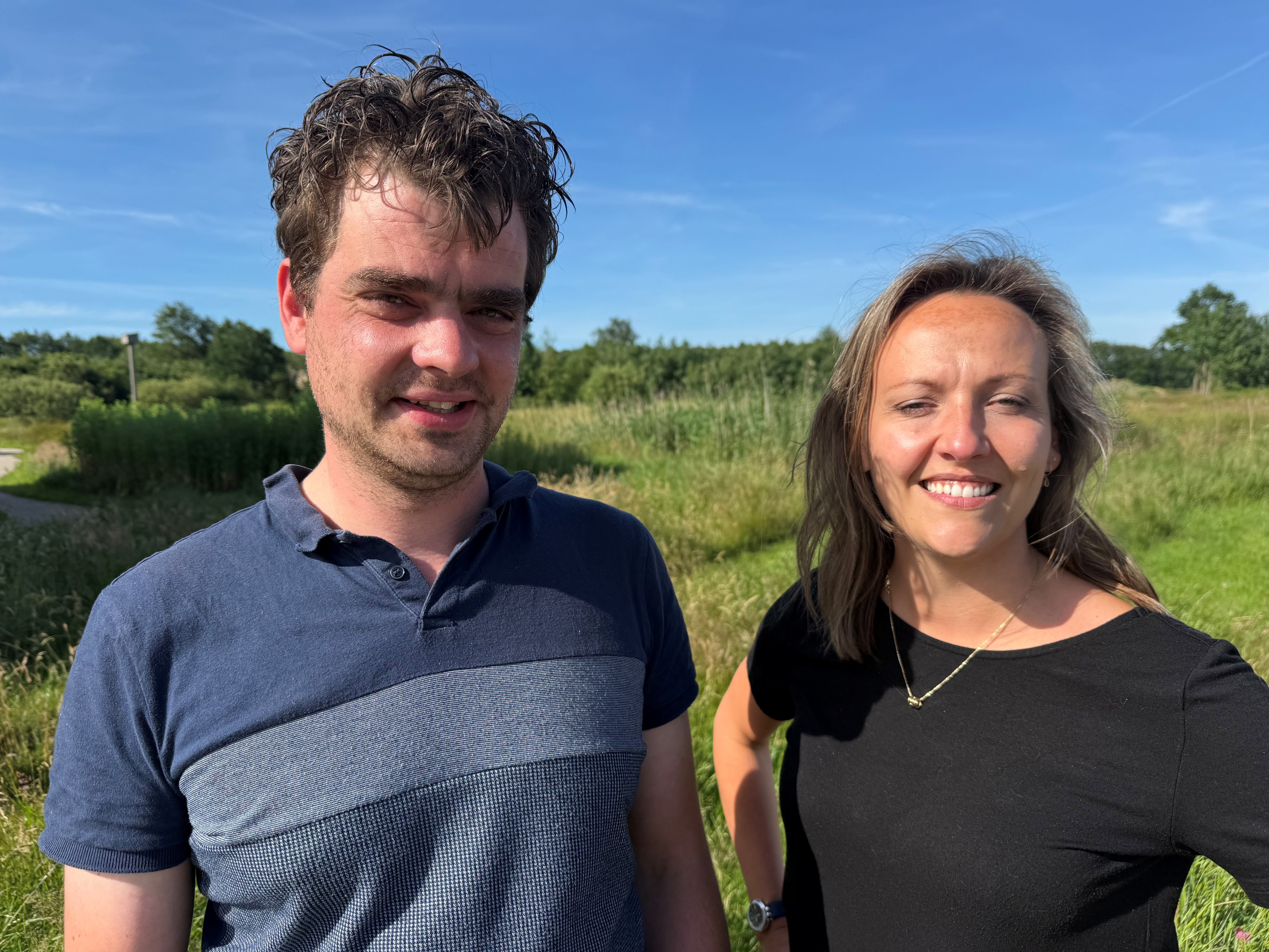 Wolvenconsulenten Robertjan en Julia staan in een groene omgeving met een mooi blauwe hemel.