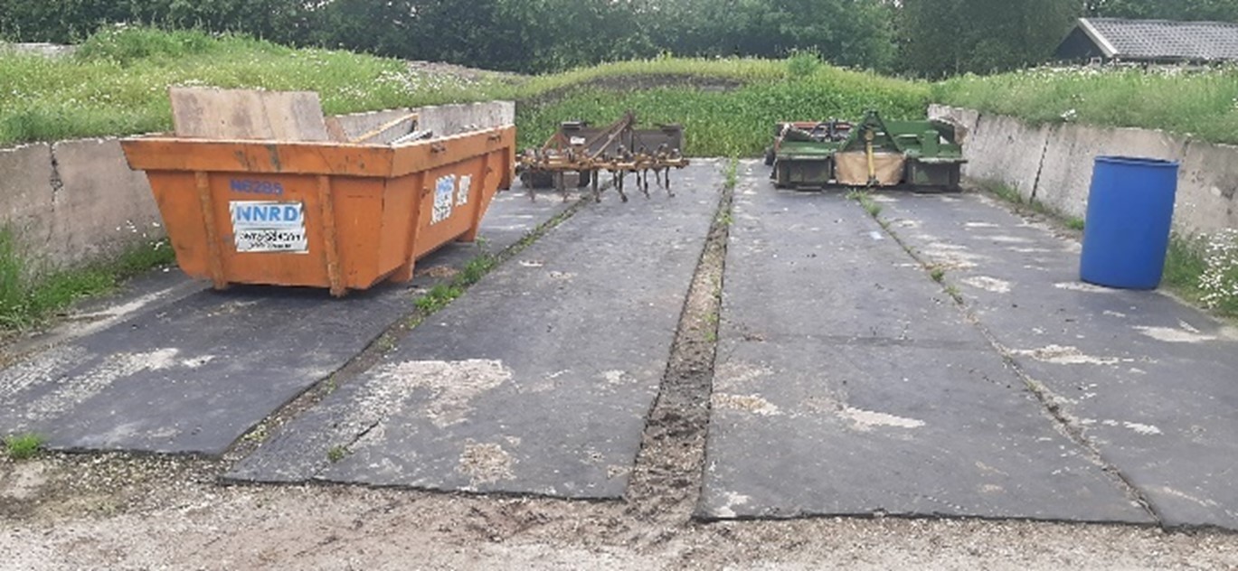 Uitgerolde rubberen matten waar een afvalcontainer op staat en nog wat andere gereedschappen.