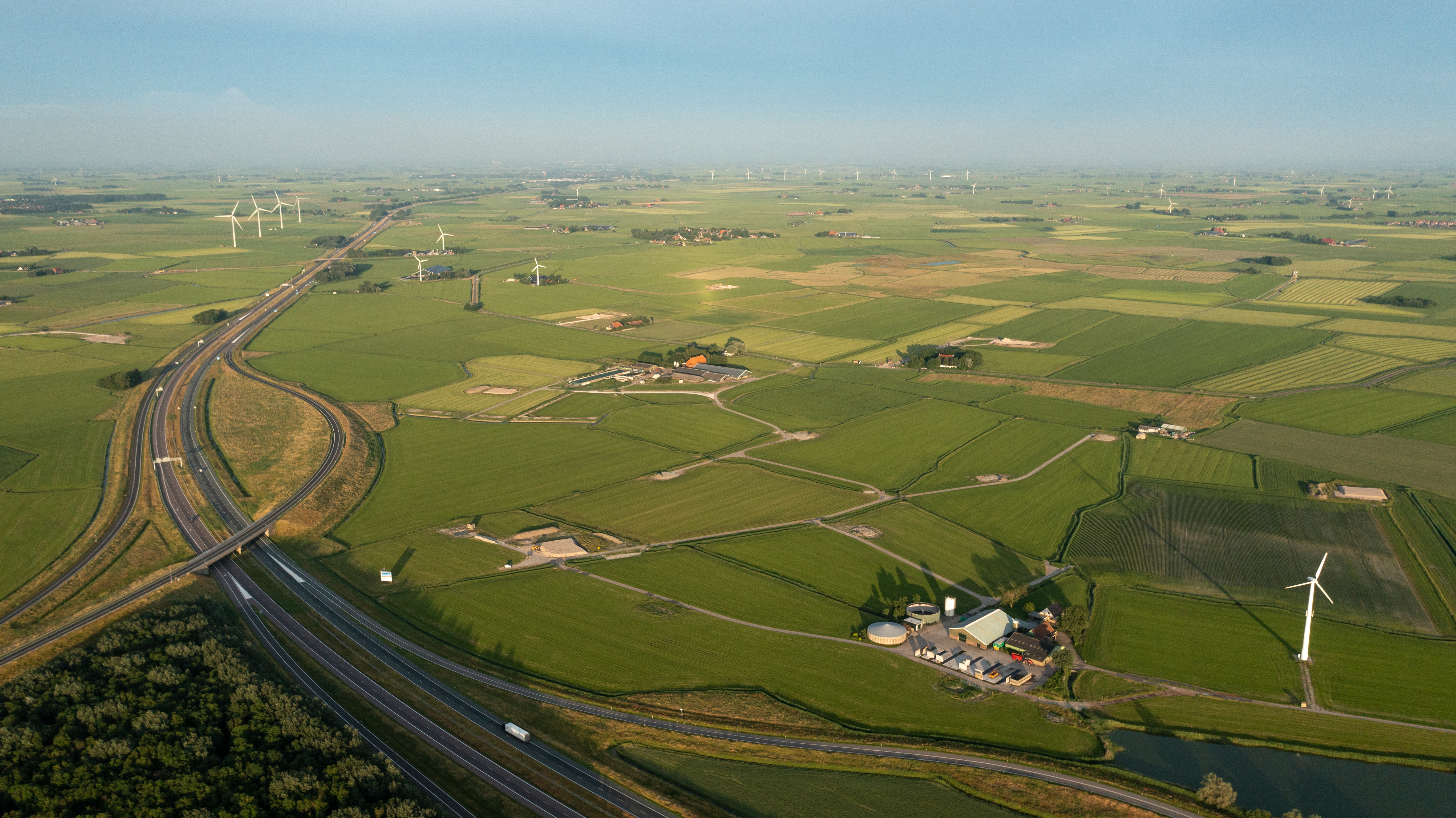 Bovenaanzicht weilanden waar wegen doorheen lopen en enkele windmolens staan.