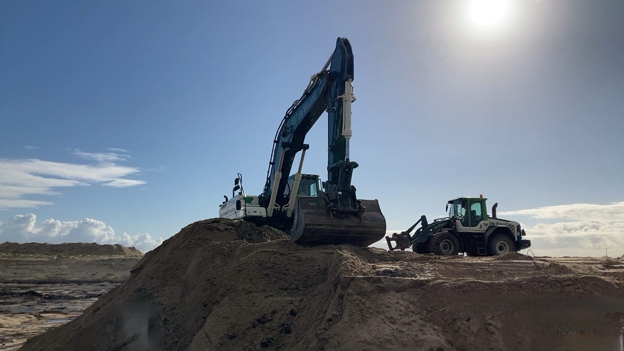 Een kraan die zand aan het scheppen is op een grote zandbult.