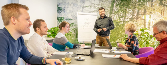 Een man staat voor een flyoverboard en er zijn 5 personen die zitten aan een tafel.