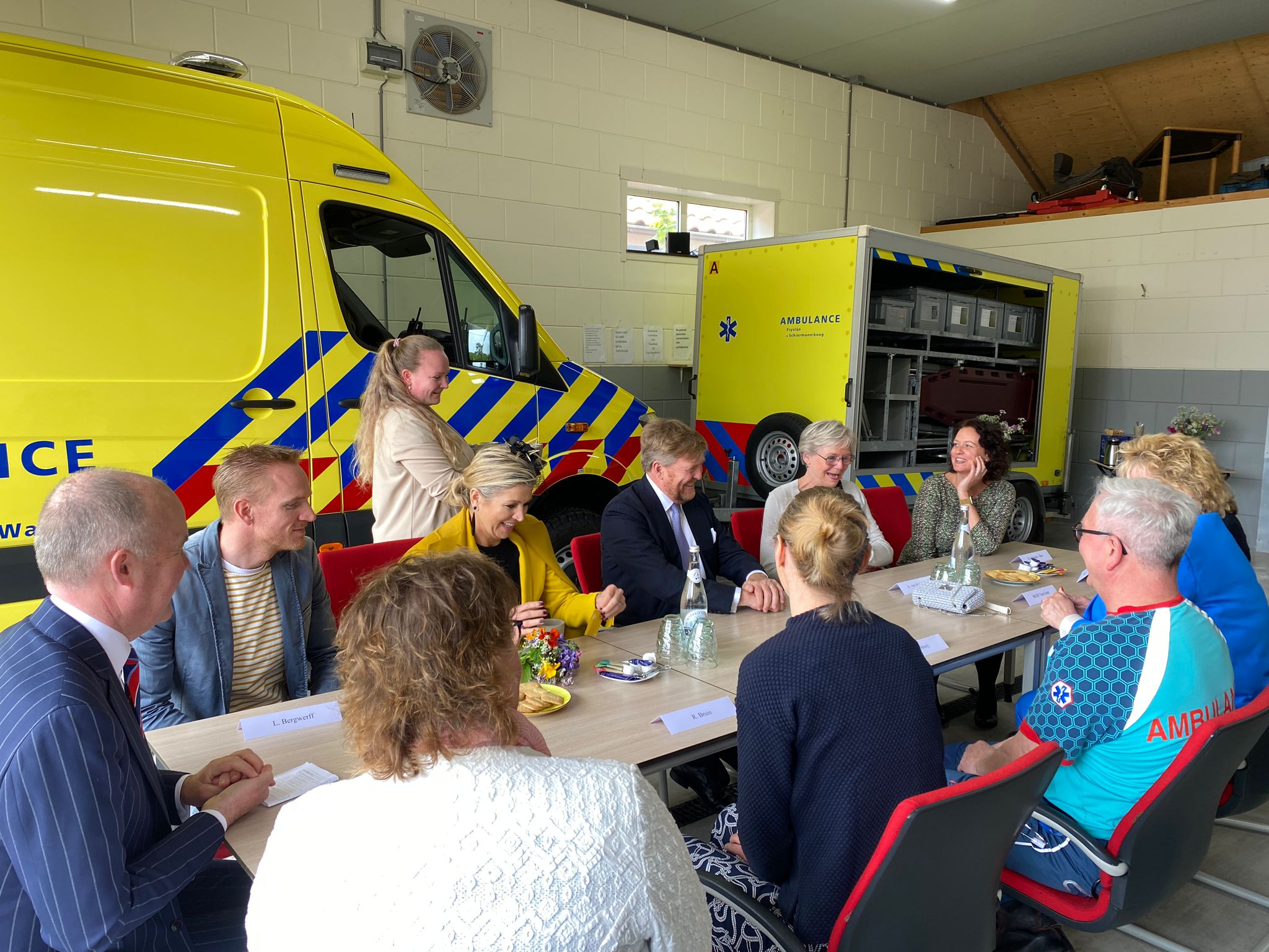 Koning en Koningin zitten in de Ambulancepost aan tafel bij ambulancepersoneel, huisartsen en fysiotherapeuten