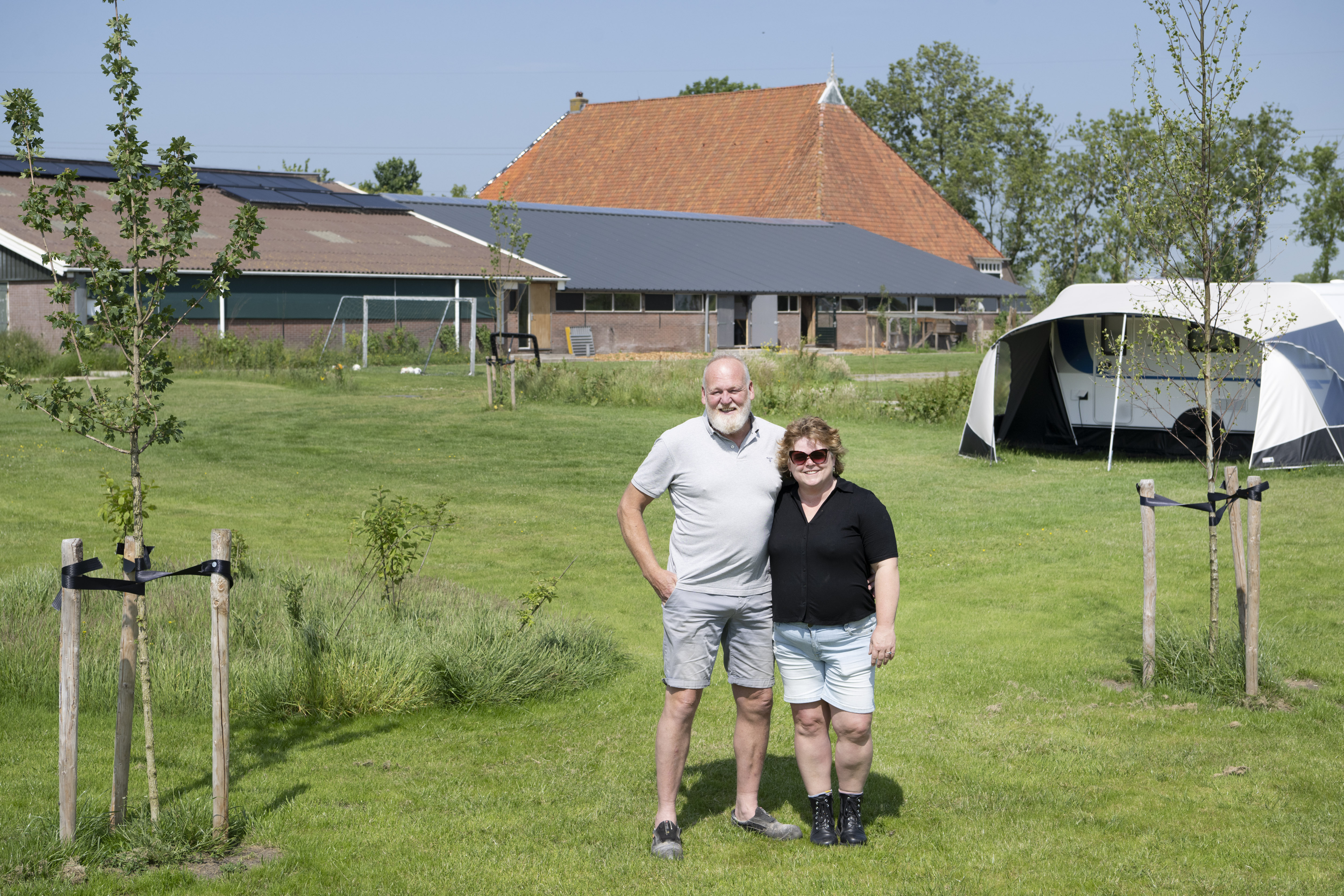 Jan-Henk en zijn vrouw Saskia in het weiland achter de boerderij en een caravan met voortent.