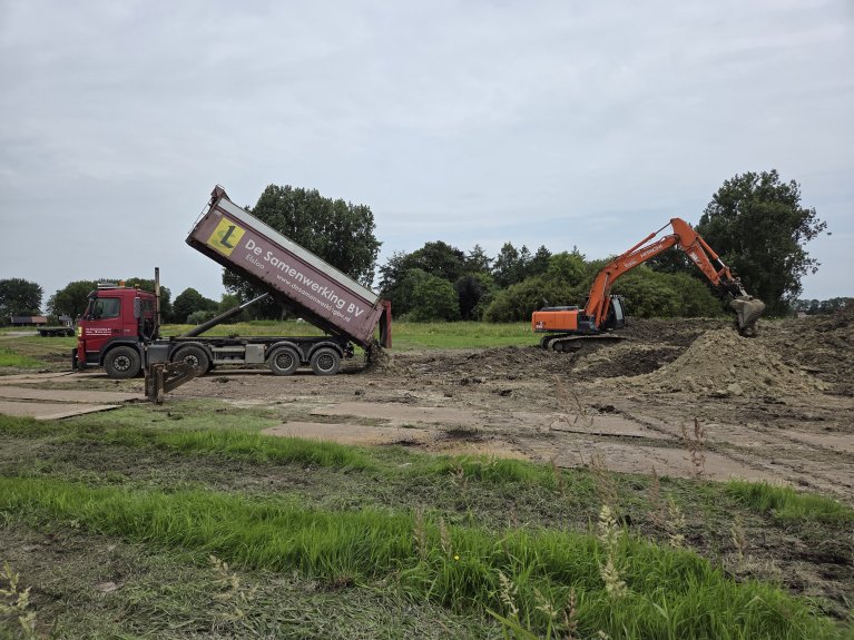 Links in beeld: een kiepwagen, rechts in beeld: een graafmachine die graaft in de grond