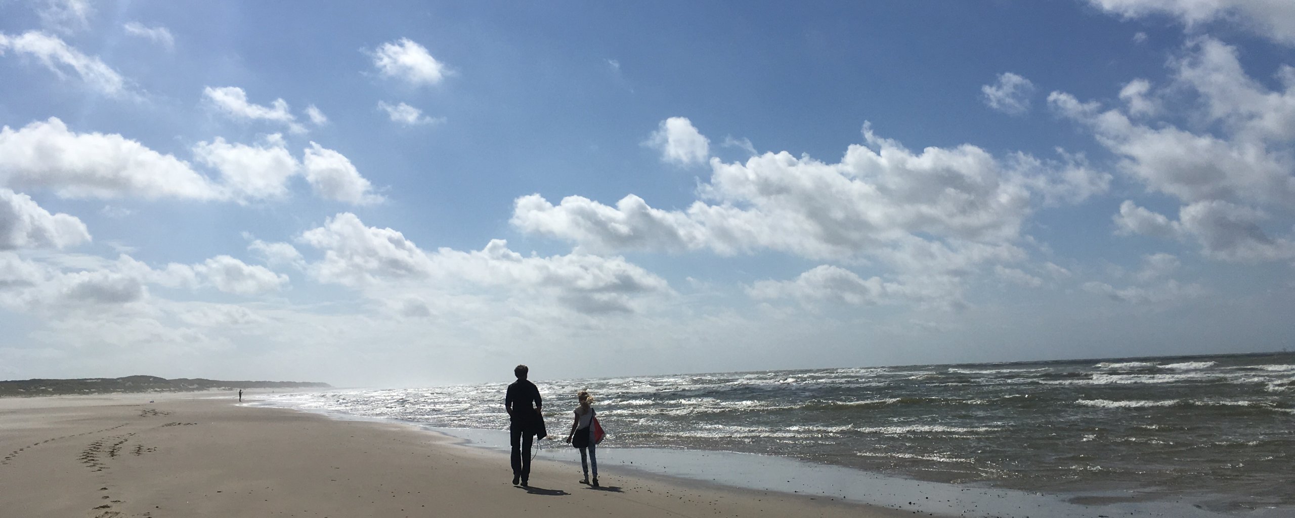 Een volwassene en een kind lopen op het strand.
