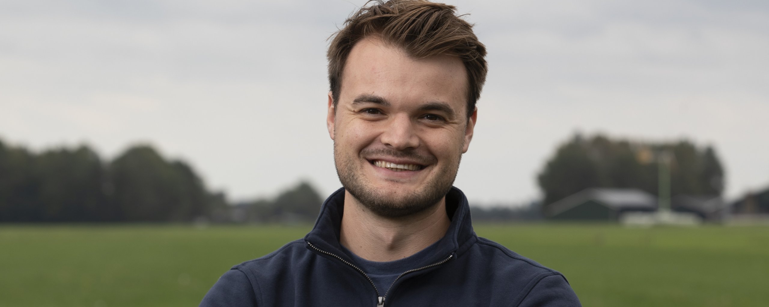 Een man staat met de armen over elkaar voor een weiland.