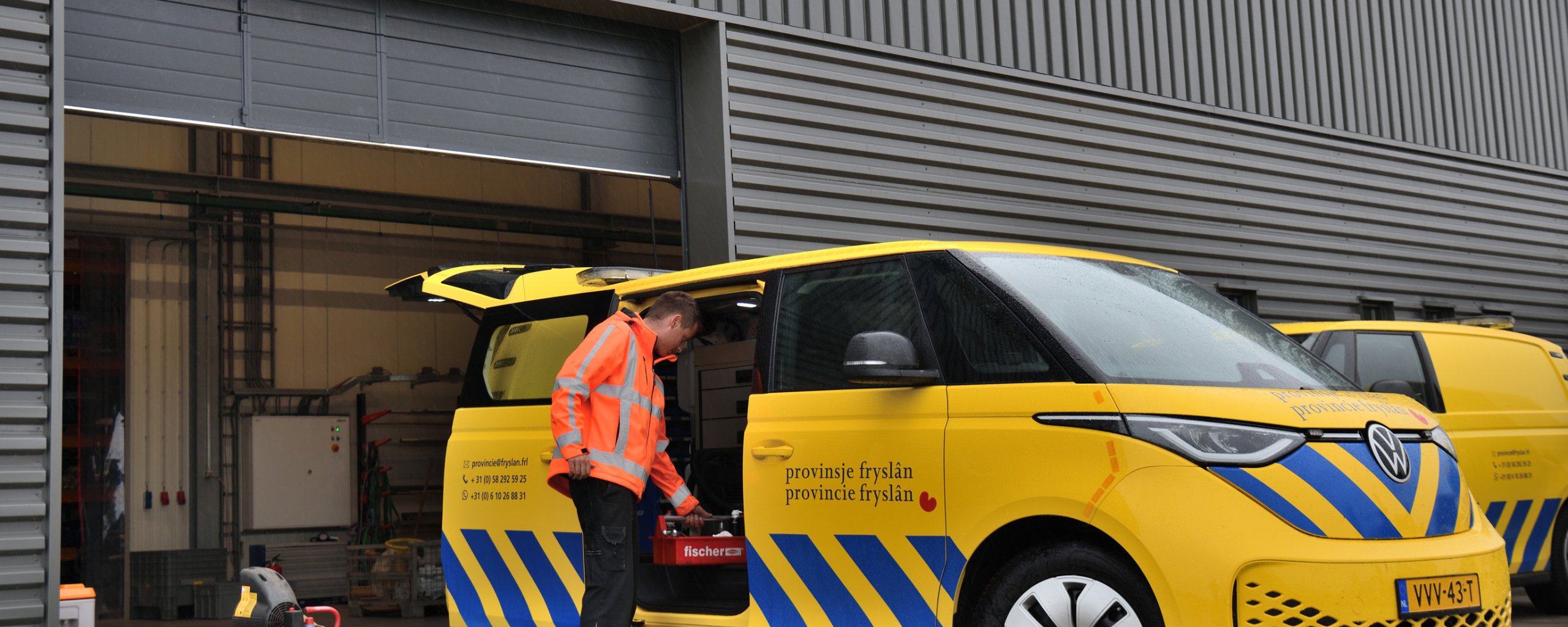 Een man in een oranje werkjas staat bij een geel VW busje van de provincie Fryslân.
