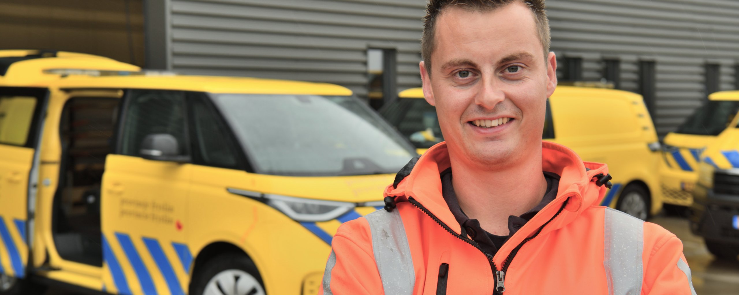Een man in een oranje werkjas staat bij een geel busje van de provincie Fryslân.