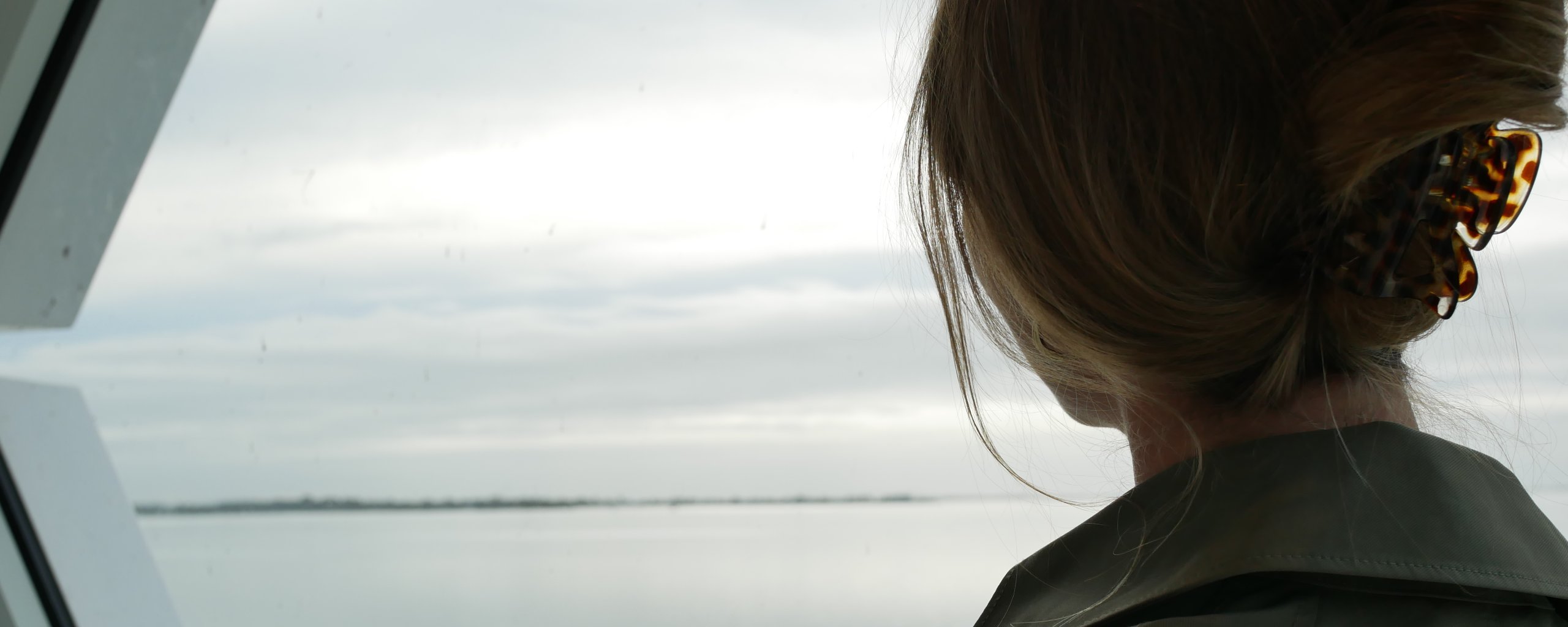 Een vrouw kijkt uit over het water vanachter een raam.