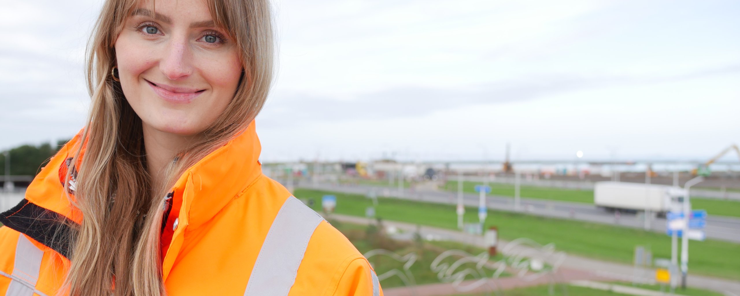 Een vrouw in een oranje werkjas staat met haar rug naar een wegenknooppunt