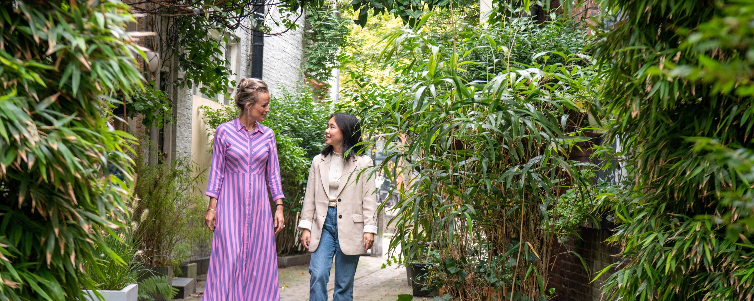 Twee vrouwen lopen op een stenen pad wat omringd is door planten.