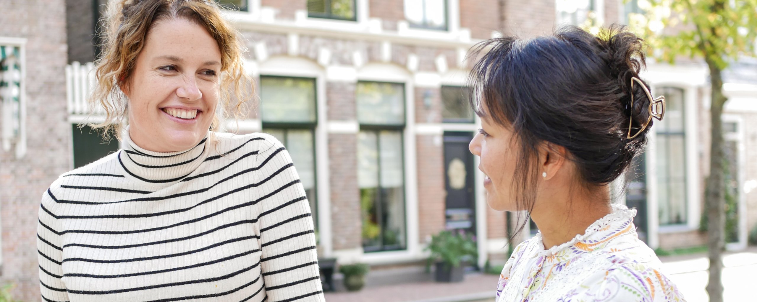 Twee vrouwen staan lachend naast elkaar bij een hekje aan de gracht.