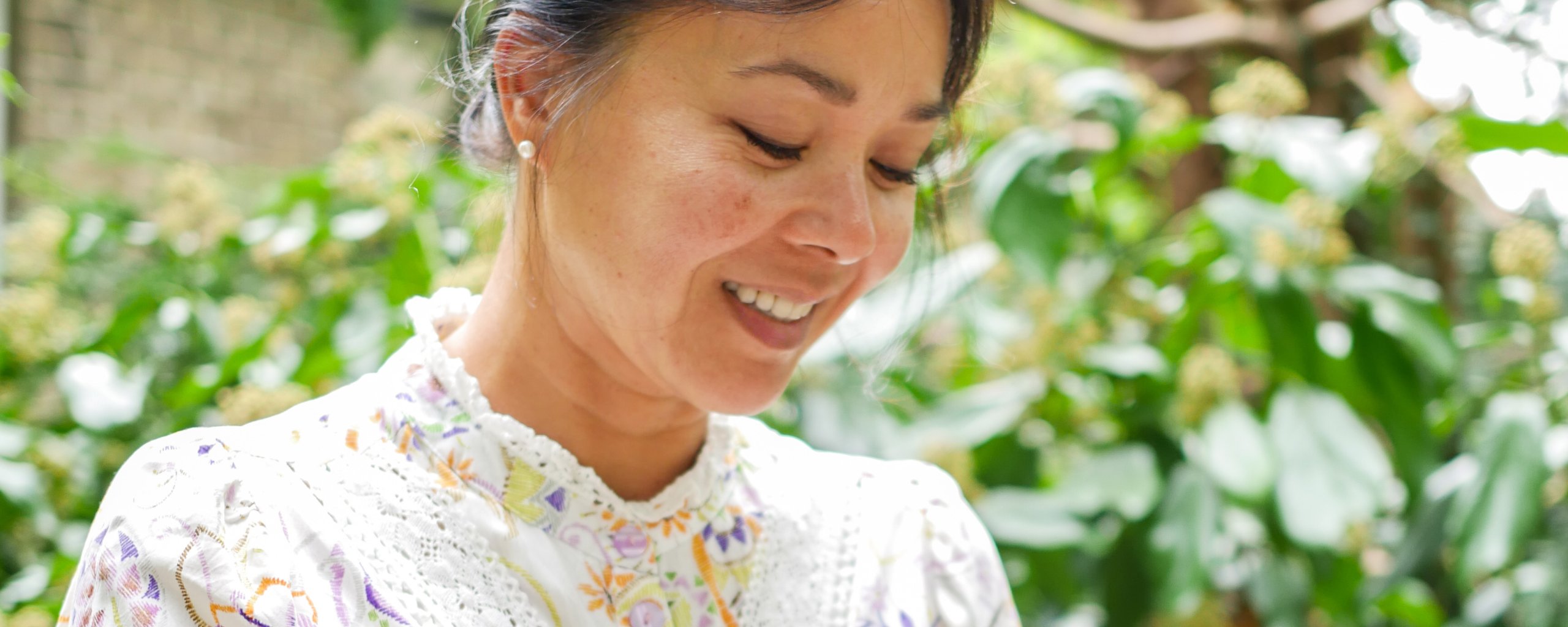 Een vrouw zit op een bankje lachend naar haar telefoon te kijken.
