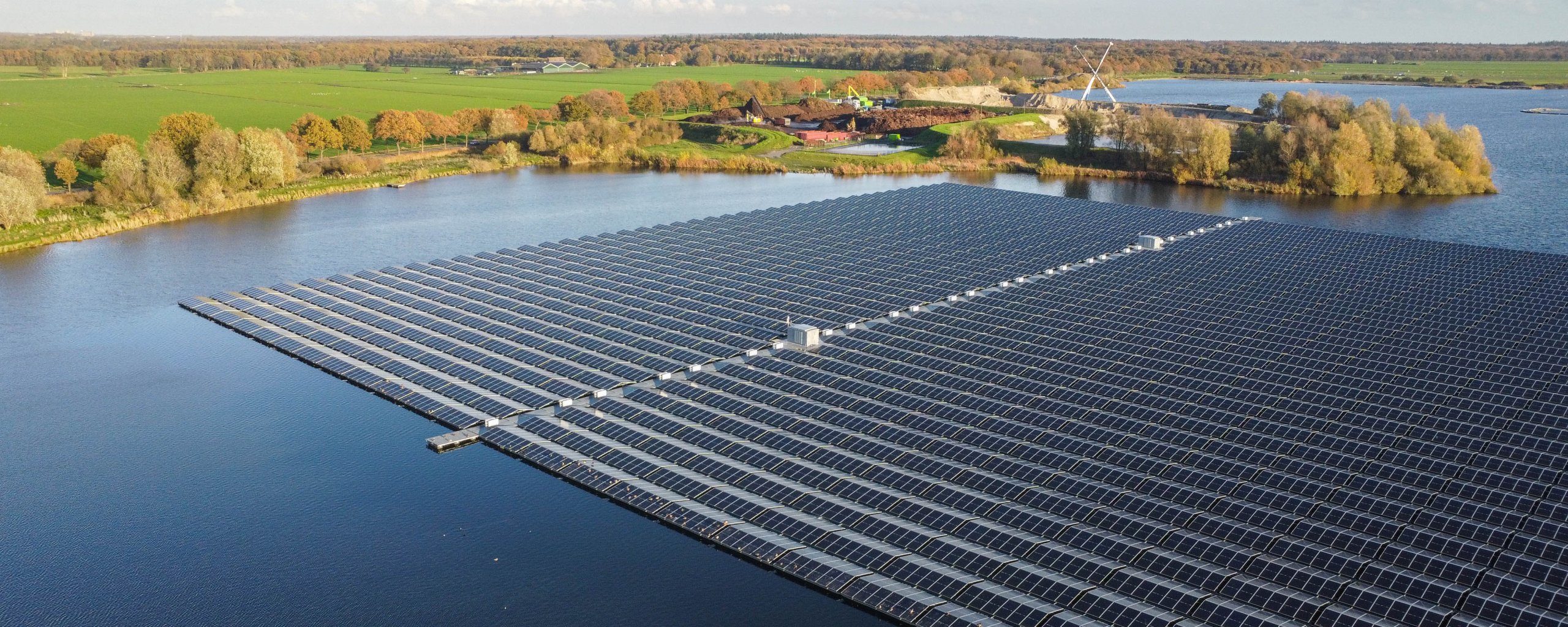 Een heel veld zonnepanelen in het water met daarom heen weilanden.