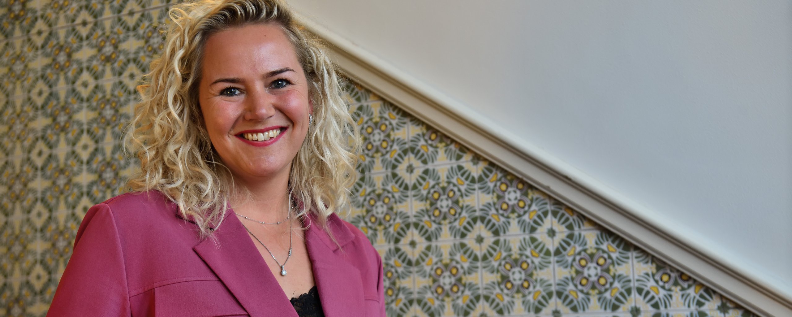 Een lachende blonde vrouw staat op een trap in het oude gedeelte van het provinciehuis.