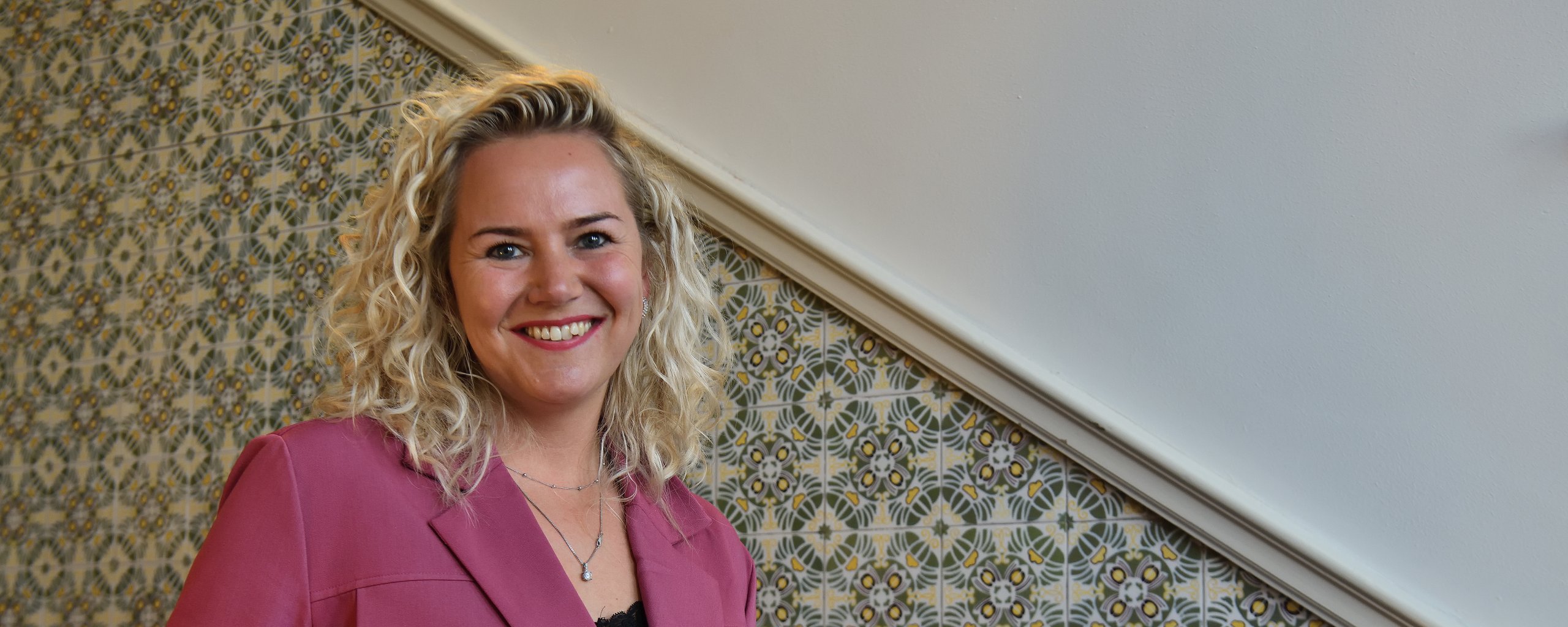 Een  blonde vrouw in een paars jasje staat op een trap