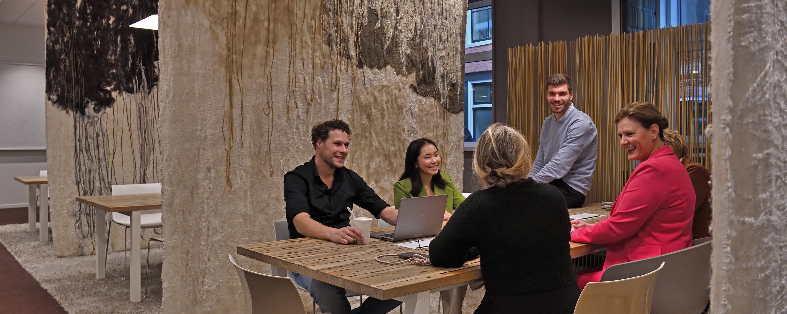 6 mensen zitten om een tafel te vergaderen met een laptop in het midden van de tafel