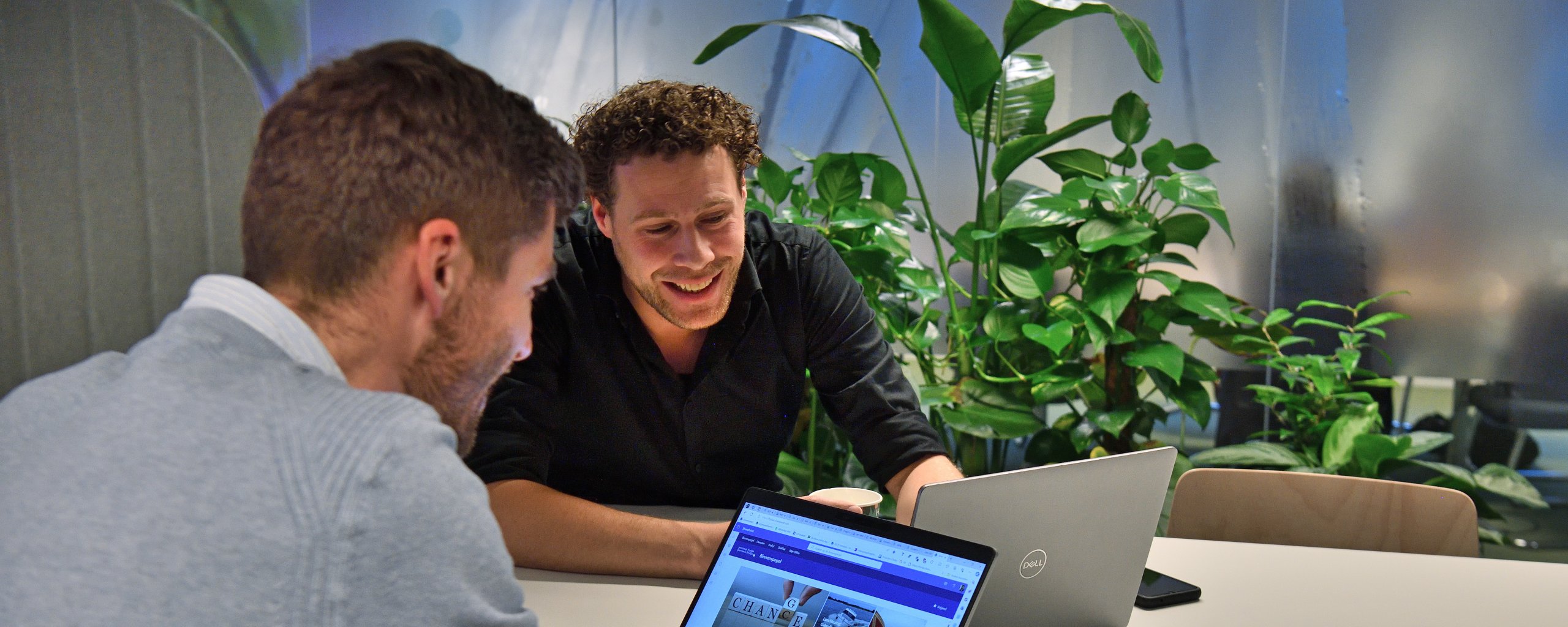 Twee personen zijn in gesprek met een open laptop voor zich.