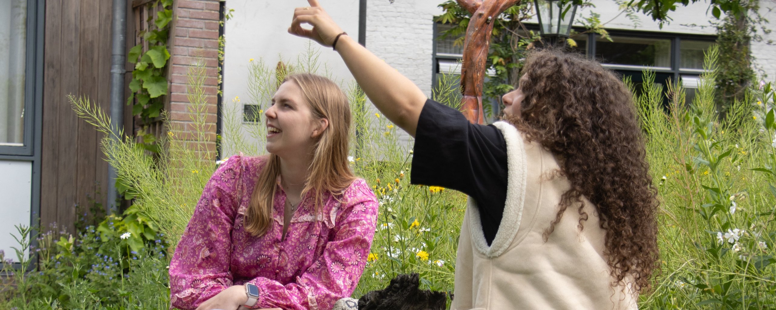 Twee vrouwen zitten aan een tafeltje. Eén van hen wijst omhoog.