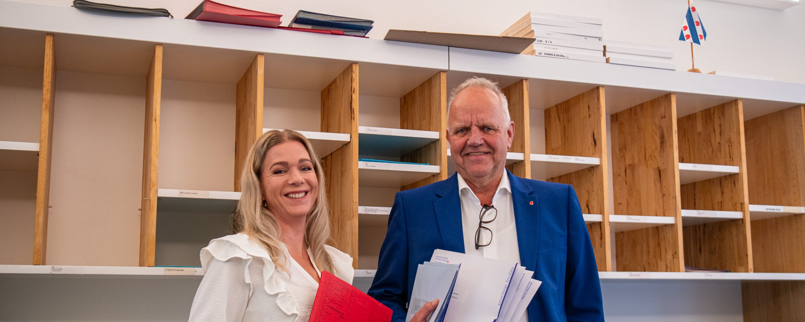 Een man en een vrouw staan lachend naast elkaar in de postkamer.