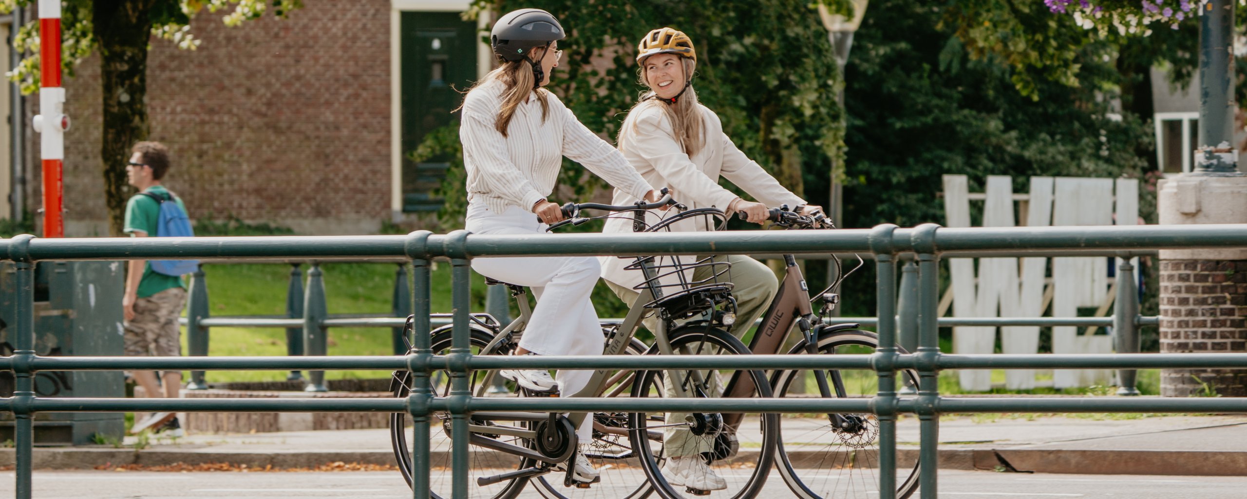 Twee vrouwen met een fietshelm op, fietsen samen over een brug