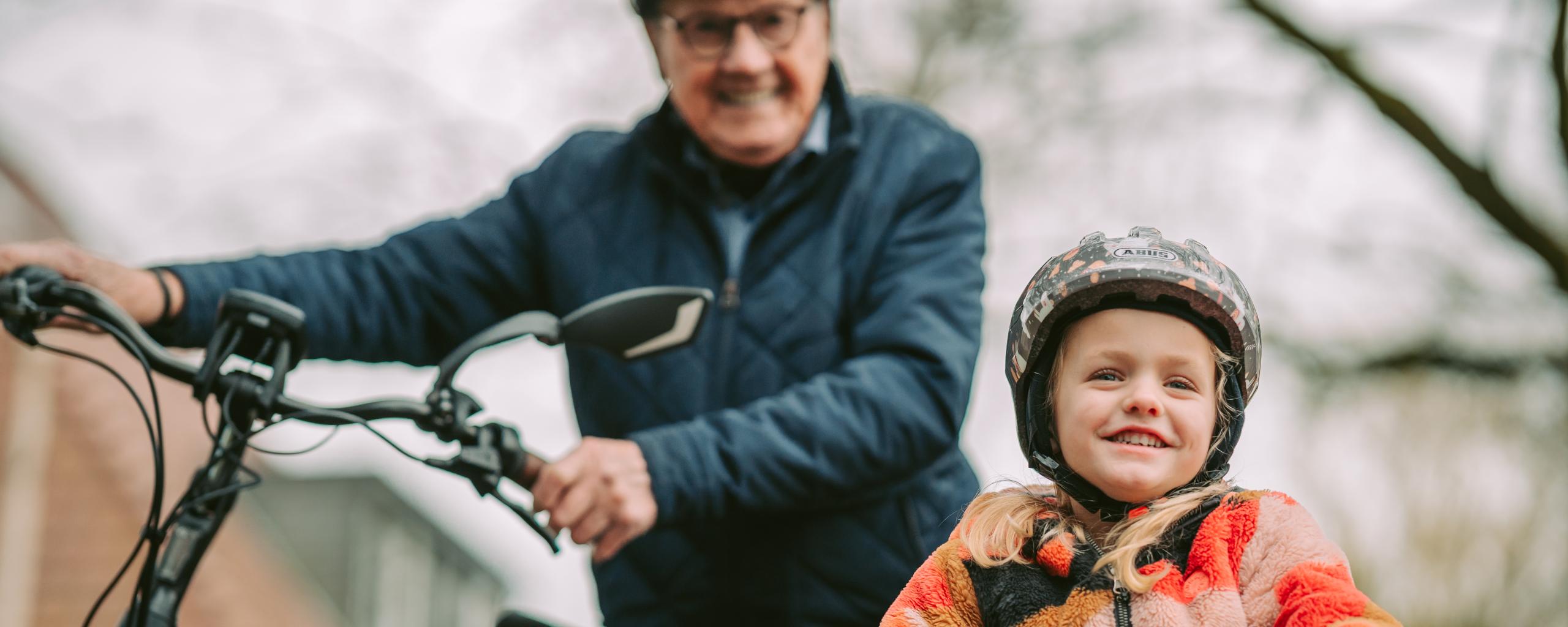 Opa met kindje op de fiets, allebei een fietshelm op