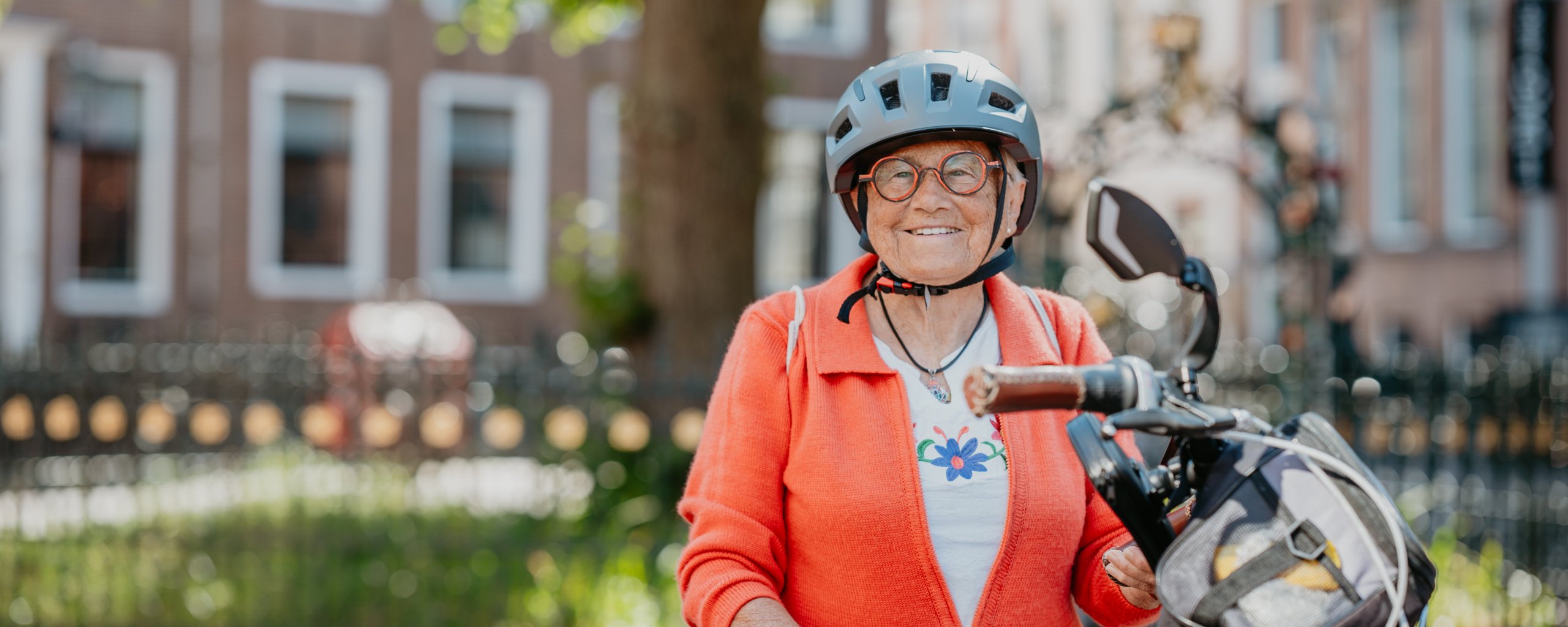 oudere dame met fietshelm op en fiets in de hand