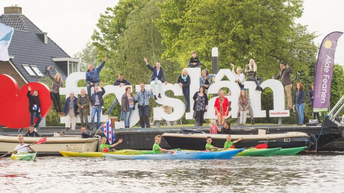 Groep mensen voor grote letters van ''Love Fryslân'  en deel van mensen in kano op het water