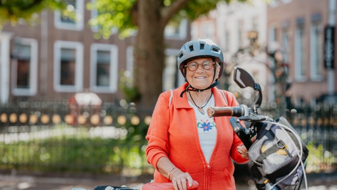 oudere dame met fietshelm op en fiets in de hand