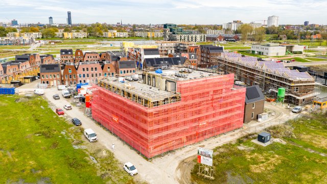 Een flat in aanbouw die helemaal in de steigers staat met oranje doeken bekleed.