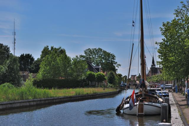 Een vaart waar een skutsje in ligt en bomen aan de oevers