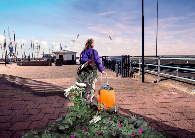 Een vrouw met een koffer die op reis gaat en een heleboel planten achter zich aan sleept.