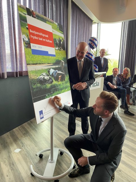 Minister Hugo de Jonge ondertekend een bord waar de voorkant van het bestjoersakkoard op afgebeeld is, Commissaris Brok staat er naast.