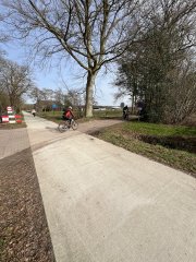 Het nieuwe betonnen fietspad waar een fietser oversteekt.