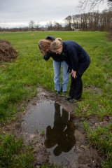 Twee vrouwen staan gebukt boven een waterplas in een weiland.