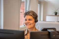 Een lachende Rixt Bekhuis met een headset op achter de computer.