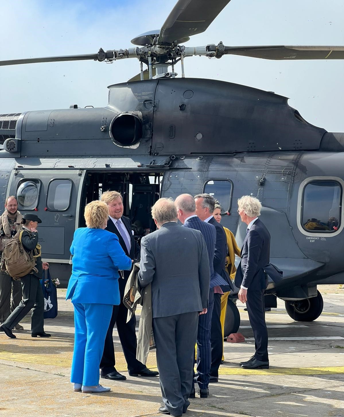 Koning en Koningin staan met meerdere mensen bij de helicopter