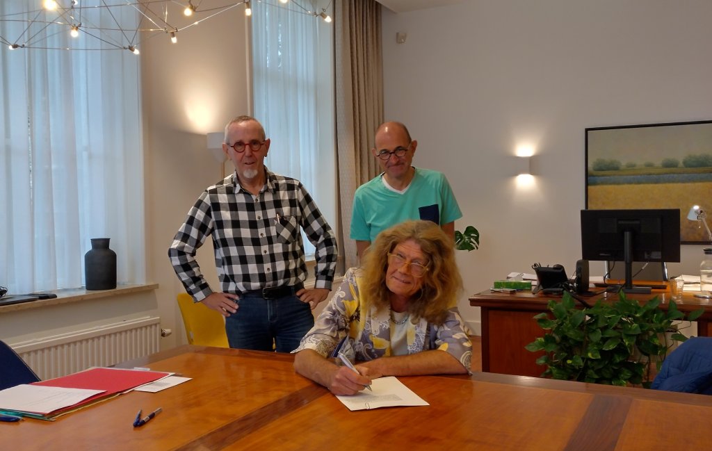 Frank/Janine, John de Bruin en Wim Schoordijk van Buurtbusvereniging Goeree-Overflakkee ondertekenen de notariële akte.